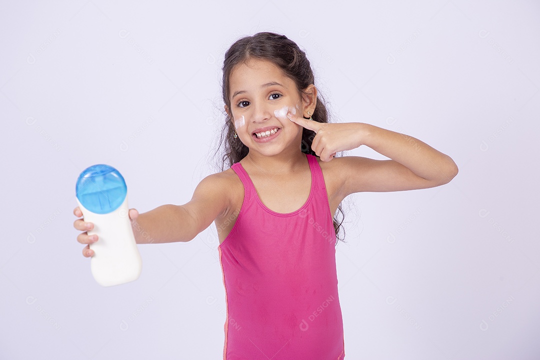 Linda garotinha sorridente com maiô segurando frasco de protetor solar