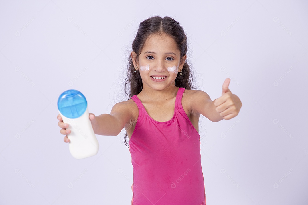 Linda garotinha sorridente com maiô segurando frasco de protetor solar