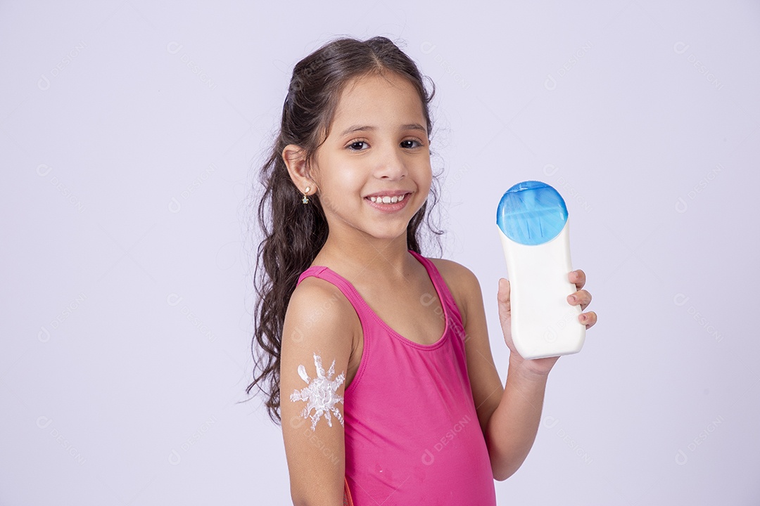 Linda garotinha sorridente com maiô segurando frasco de protetor solar