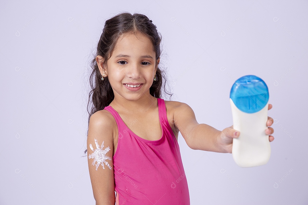 Linda garotinha sorridente com maiô segurando frasco de protetor solar
