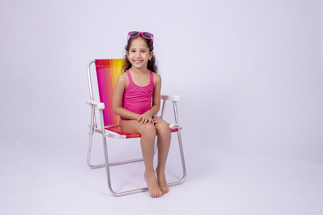 Linda garotinha sorridente com óculos de sol e maiô sentada na cadeira de praia
