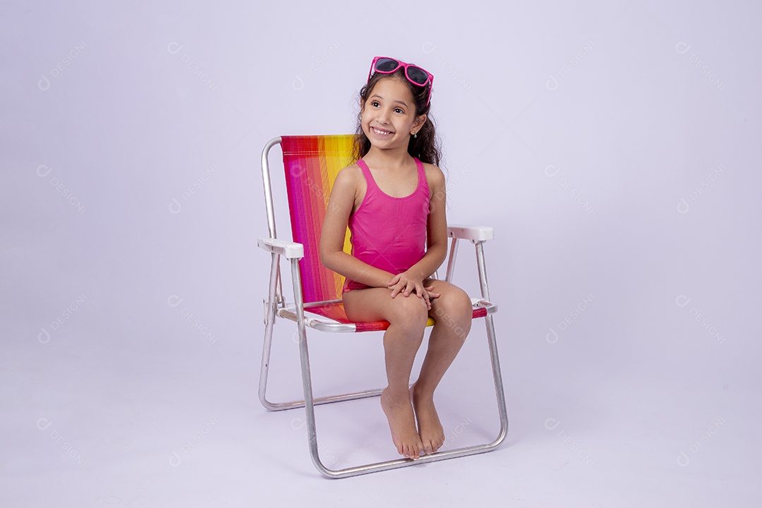 Linda garotinha sorridente com óculos de sol e maiô sentada na cadeira de praia