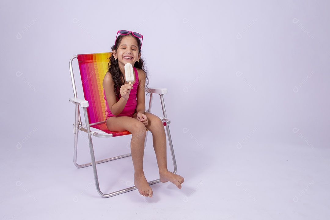 Linda garotinha sorridente com óculos de sol e maiô sentada na cadeira de praia