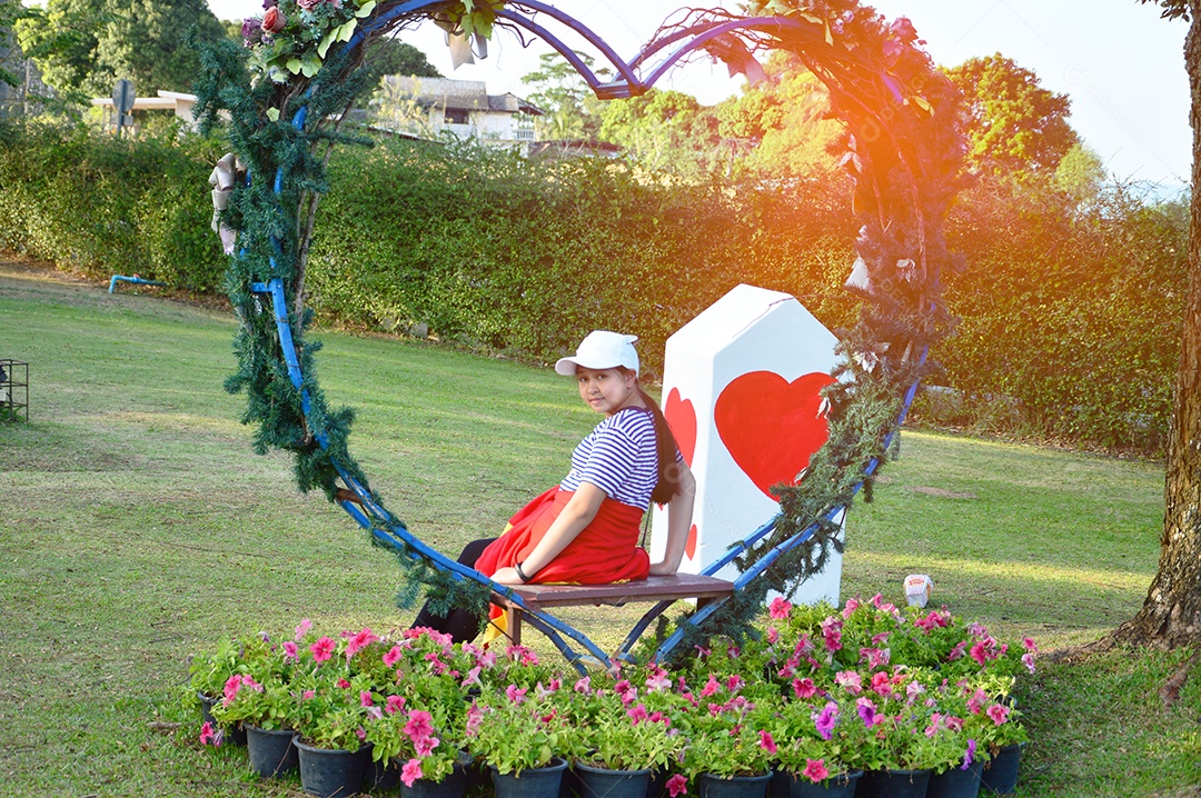 Linda garota sentada sobre banco de coração no jardim