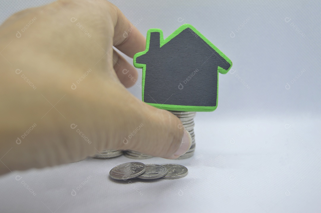 Miniatura de uma casa com moedas empilhadas em fundo branco