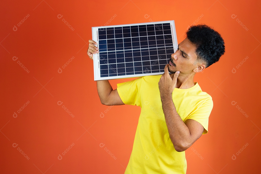 Homem negro segurando um painel solar isolado em laranja.