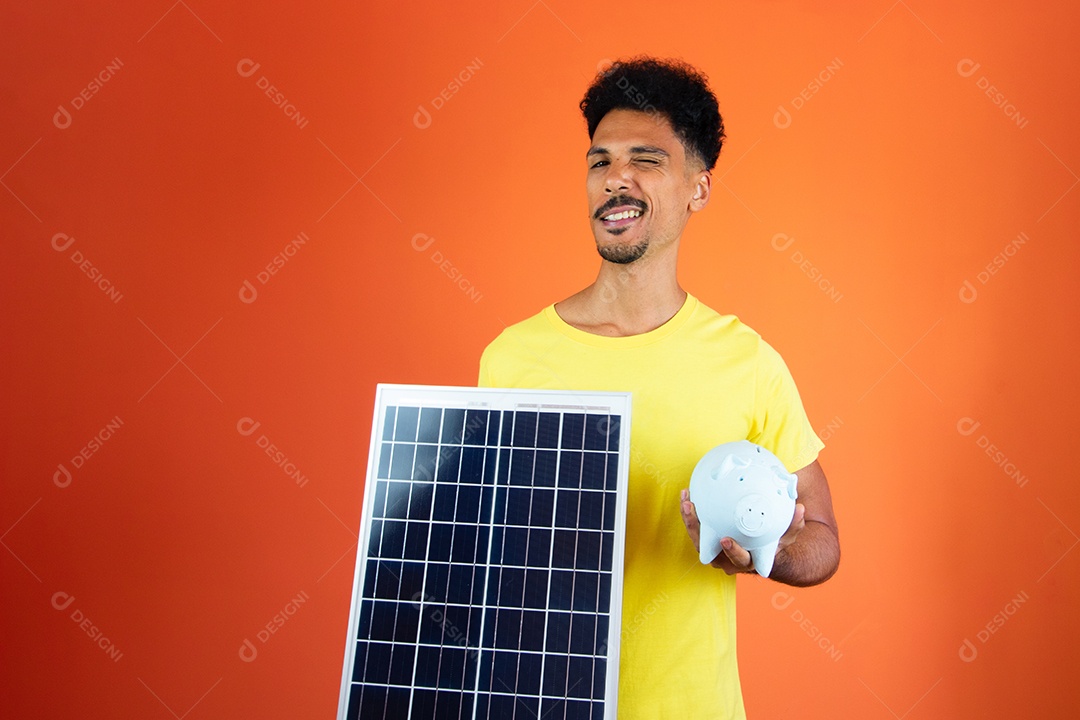 Homem negro segurando um cofrinho e painel solar isolado em laranja.