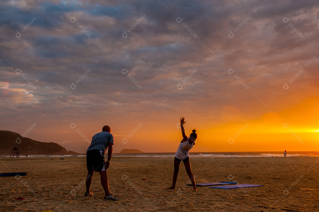 Jovens se alongando na praia ao pôr do sol