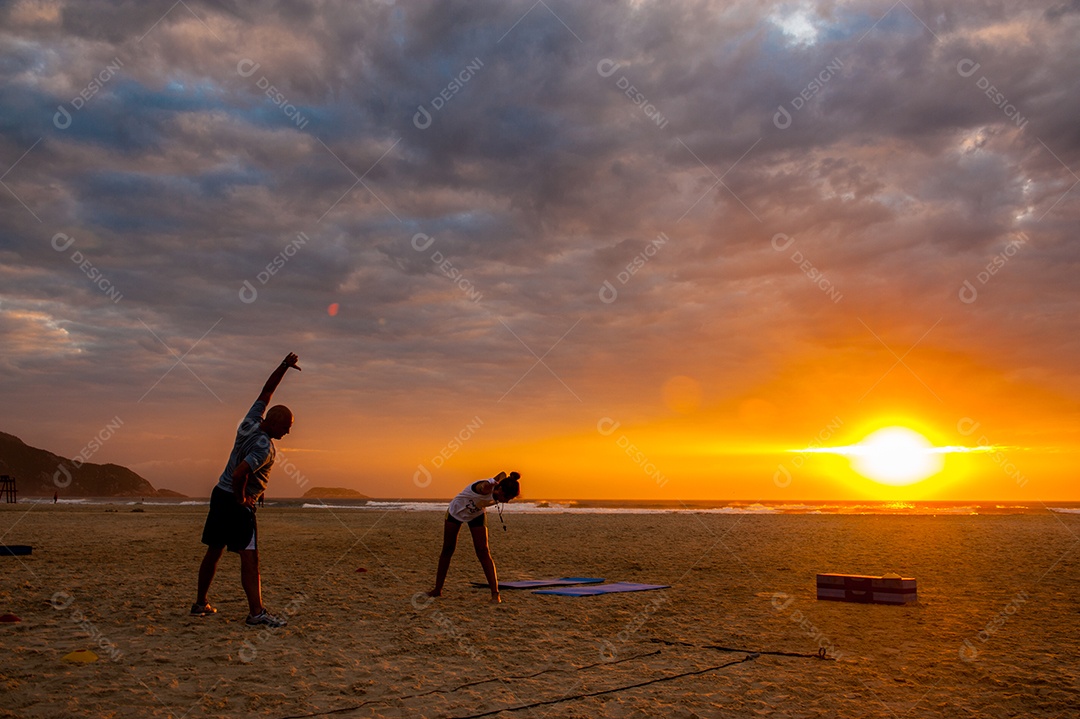 Jovens se alongando na praia ao pôr do sol