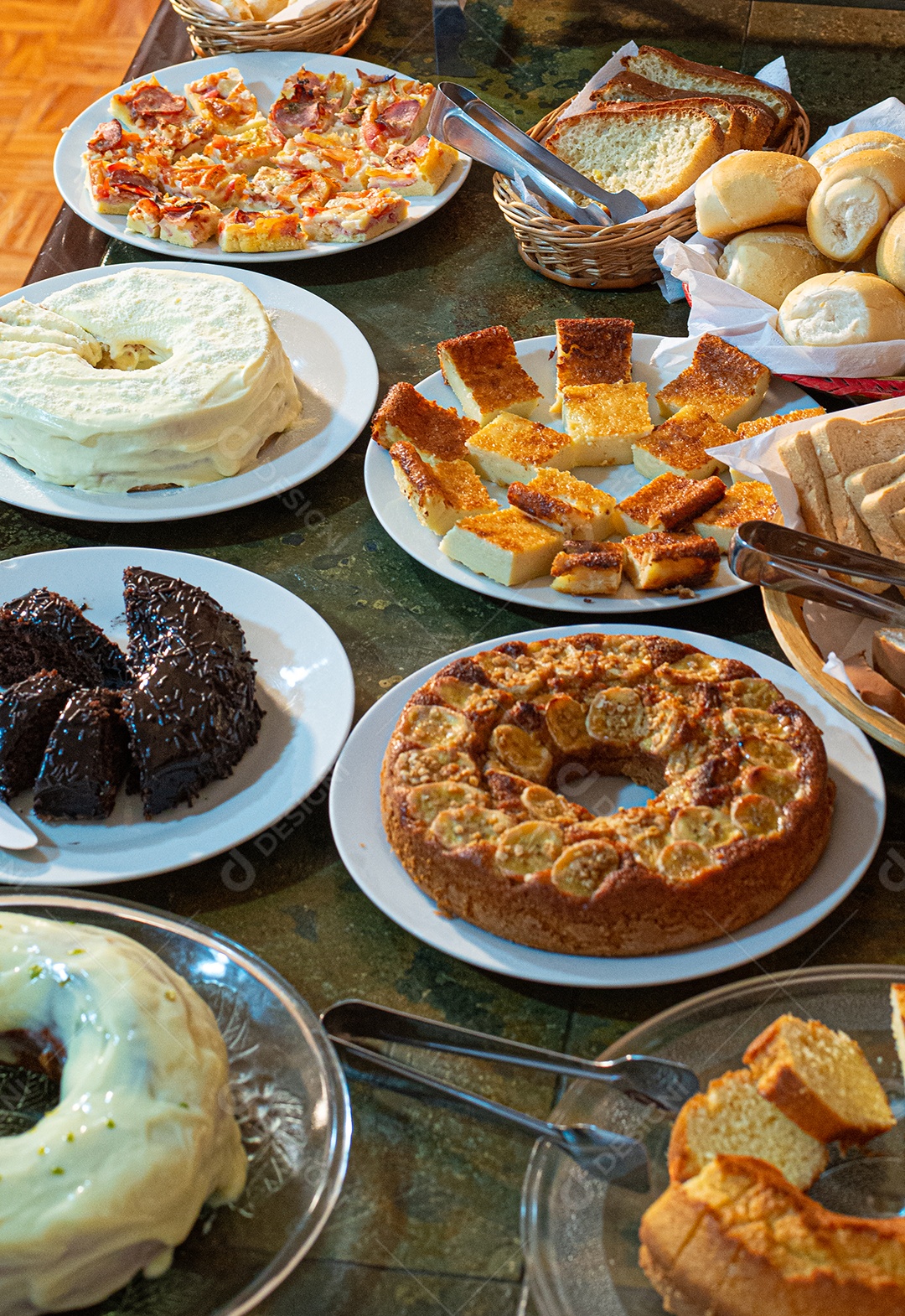 Café da manhã farto servido com bolos, tortas, geléias, doces, queijos, presunto, café, leite.