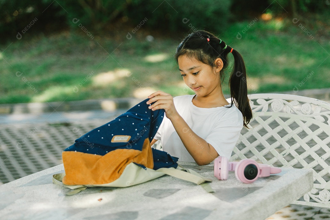 Garotinha sentada na mesa com materiais na mochila