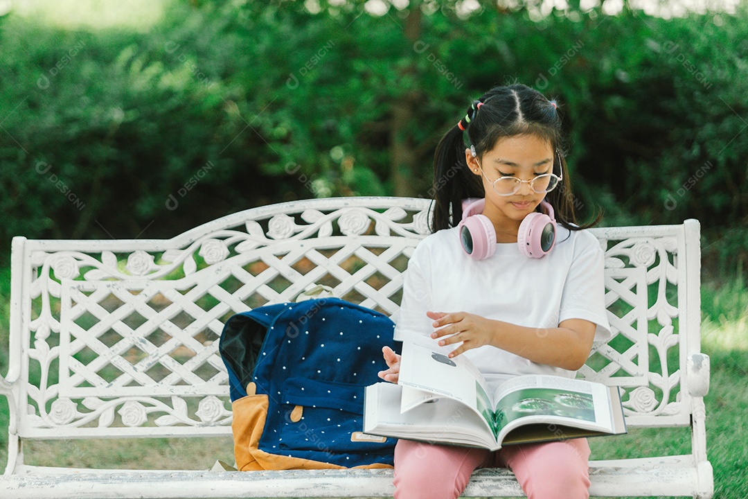 Garotinha bonita sentada no banco lendo livro