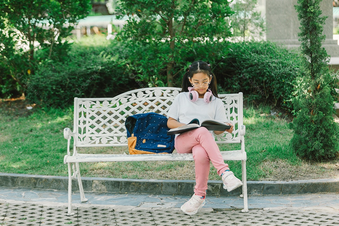 Garotinha bonita sentada no banco lendo livro