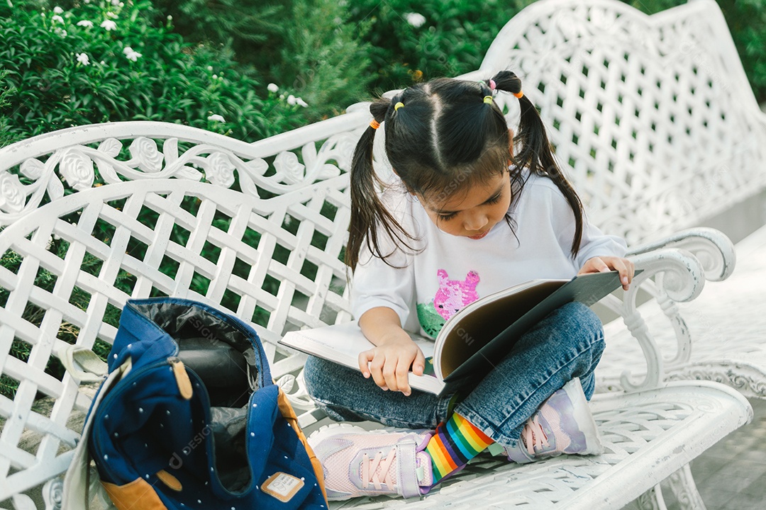Garotinha bonita sentada no banco lendo livro