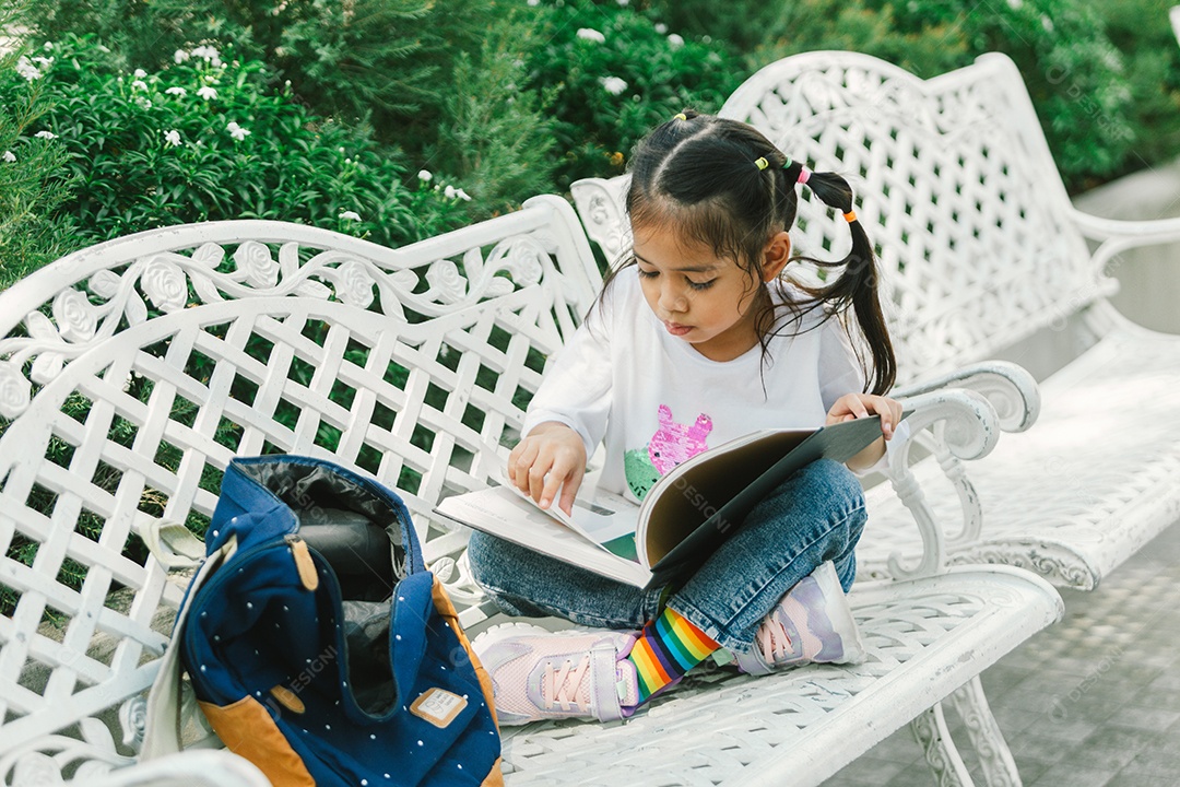 Garotinha bonita sentada no banco lendo livro