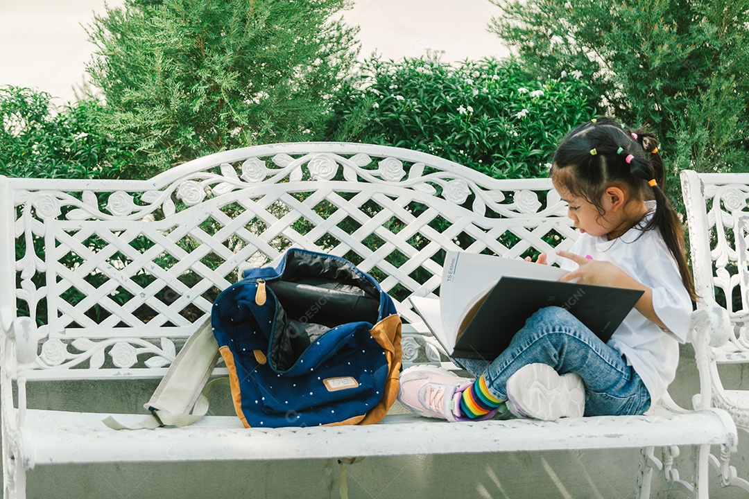 Garotinha bonita sentada no banco lendo livro