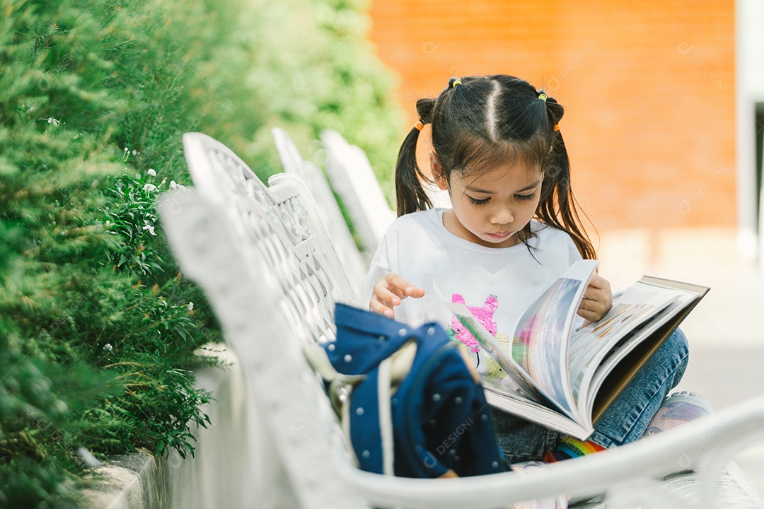Garotinha bonita sentada no banco lendo livro