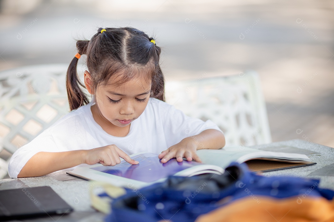 De volta à escola. Menina asiática lendo um livro. Alunos do ensino fundamental depois das aulas aprendendo lição de casa.