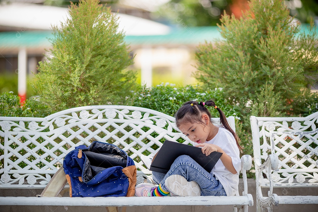De volta à escola. Menina asiática lendo um livro. Alunos do ensino fundamental depois das aulas aprendendo lição de casa.