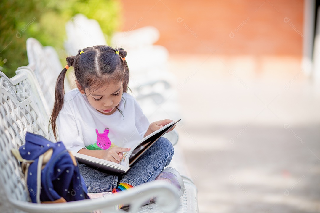De volta à escola. Menina asiática lendo um livro. Alunos do ensino fundamental depois das aulas aprendendo lição de casa.