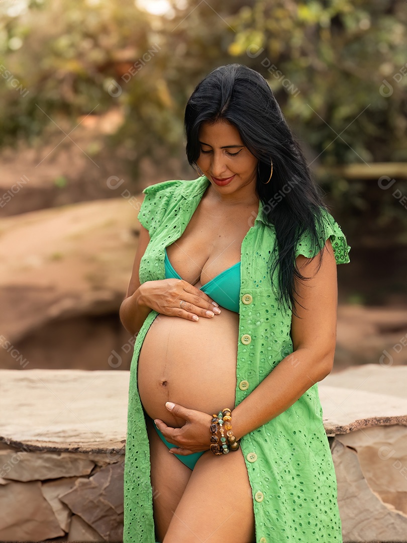 Grávida em ambiente natural com pedras segurando a barriga