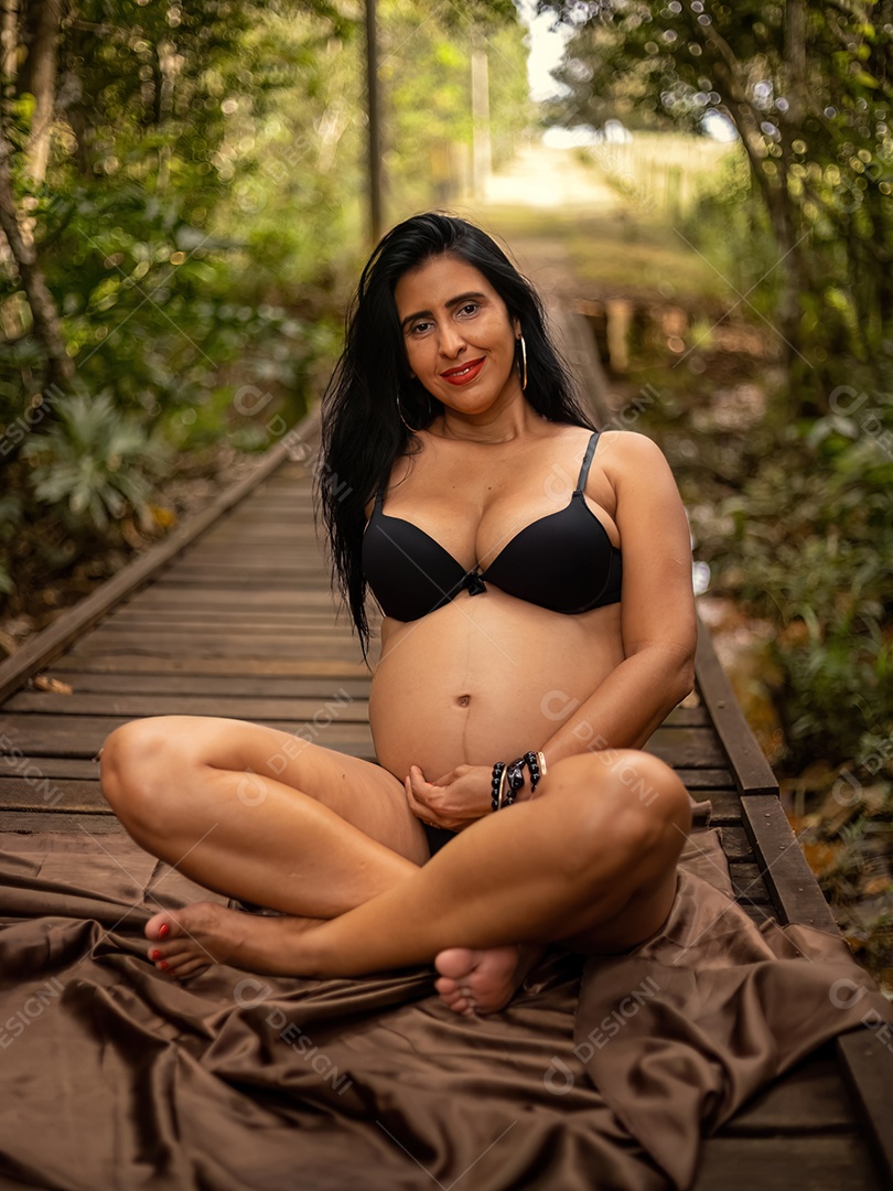 Mulher grávida posando em sessão de fotos feminina deitada em uma ponte de madeira