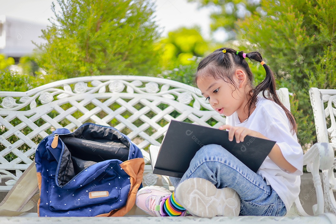 Menina asiática lendo um livro depois das aulas aprendendo lição de casa