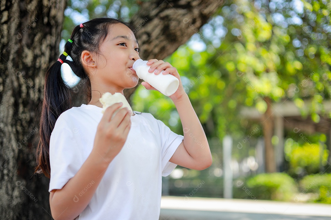 Garotinha asiática segurando e comendo pão na escola.