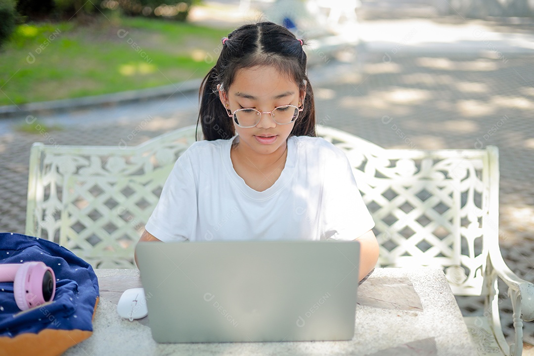 Garotinha asiática usa um laptop para aprender na escola.