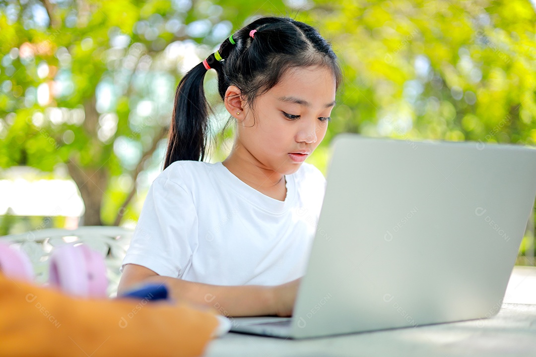 Garotinha asiática usa um laptop para aprender na escola.
