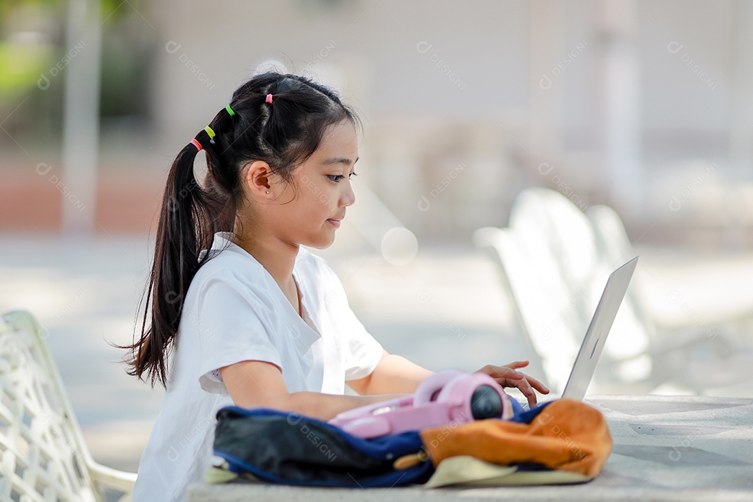 Garotinha asiática usa um laptop para aprender na escola.