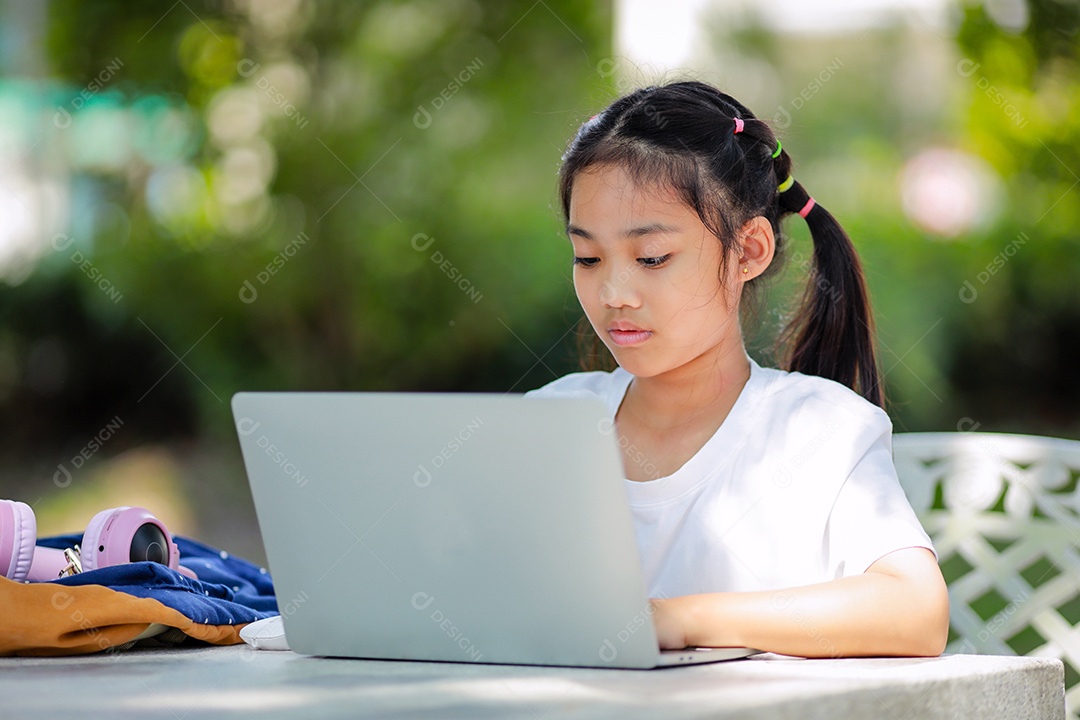 Garotinha asiática usa um laptop para aprender na escola.