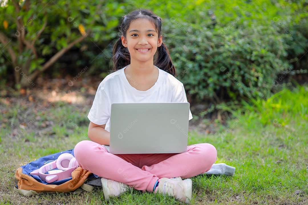 Garotinha asiática usa um laptop para aprender na escola.