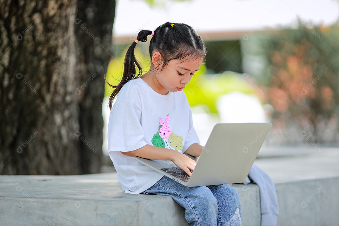 Garotinha asiática usa um laptop para aprender na escola.