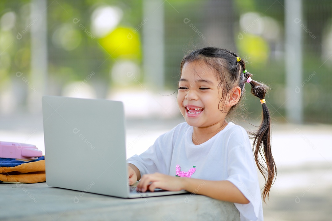 Garotinha asiática usa um laptop para aprender na escola.