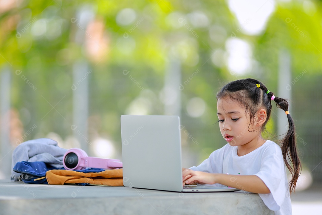 Garotinha asiática usa um laptop para aprender na escola.