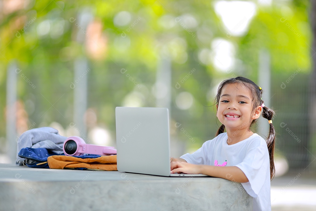 Garotinha asiática usa um laptop para aprender na escola.