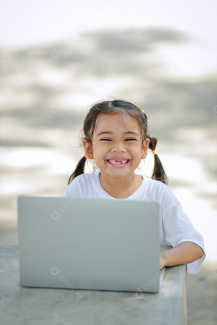 Garotinha asiática usa um laptop para aprender na escola.