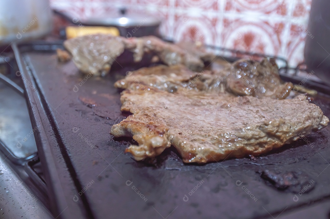 Conceito de churrasco em casa, carne sendo preparada em uma placa de fogão caseira
