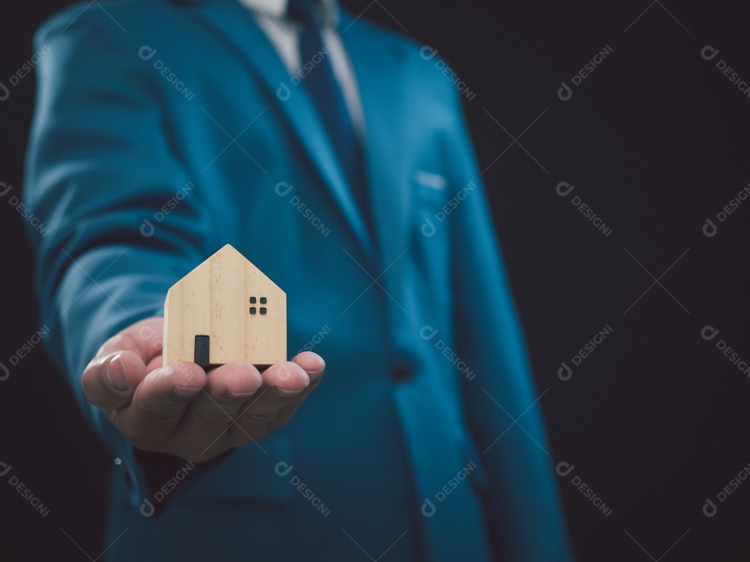 Conceito de vender uma casa. Empresário está segurando uma casa modelo em um fundo escuro. Agente imobiliário oferece casa, seguro de propriedade e segurança, conceitos de habitação a preços acessíveis, corretor de seguros residenciais, vendedor.