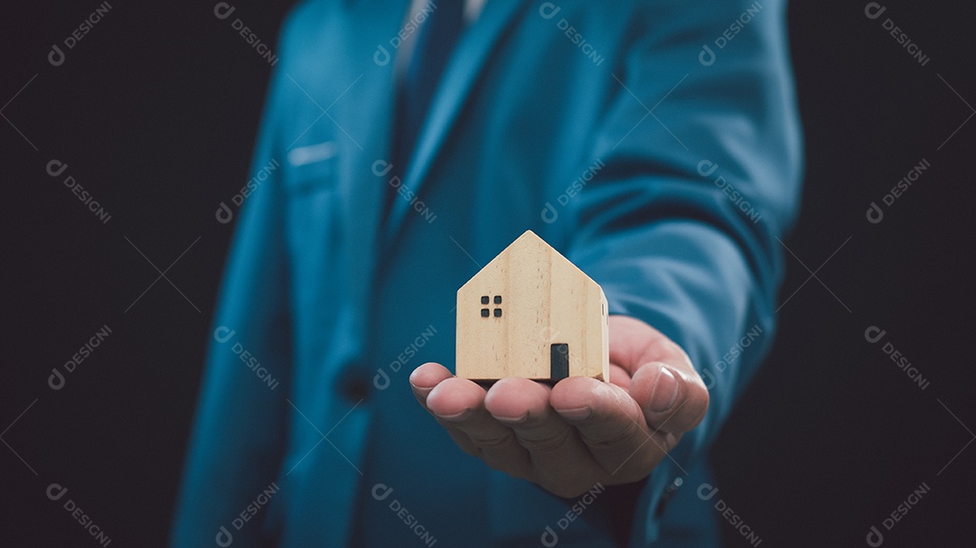 Conceito de vender uma casa. Empresário está segurando uma casa modelo em um fundo escuro. Agente imobiliário oferece casa, seguro de propriedade e segurança, conceitos de habitação a preços acessíveis, corretor de seguros residenciais, vendedor.