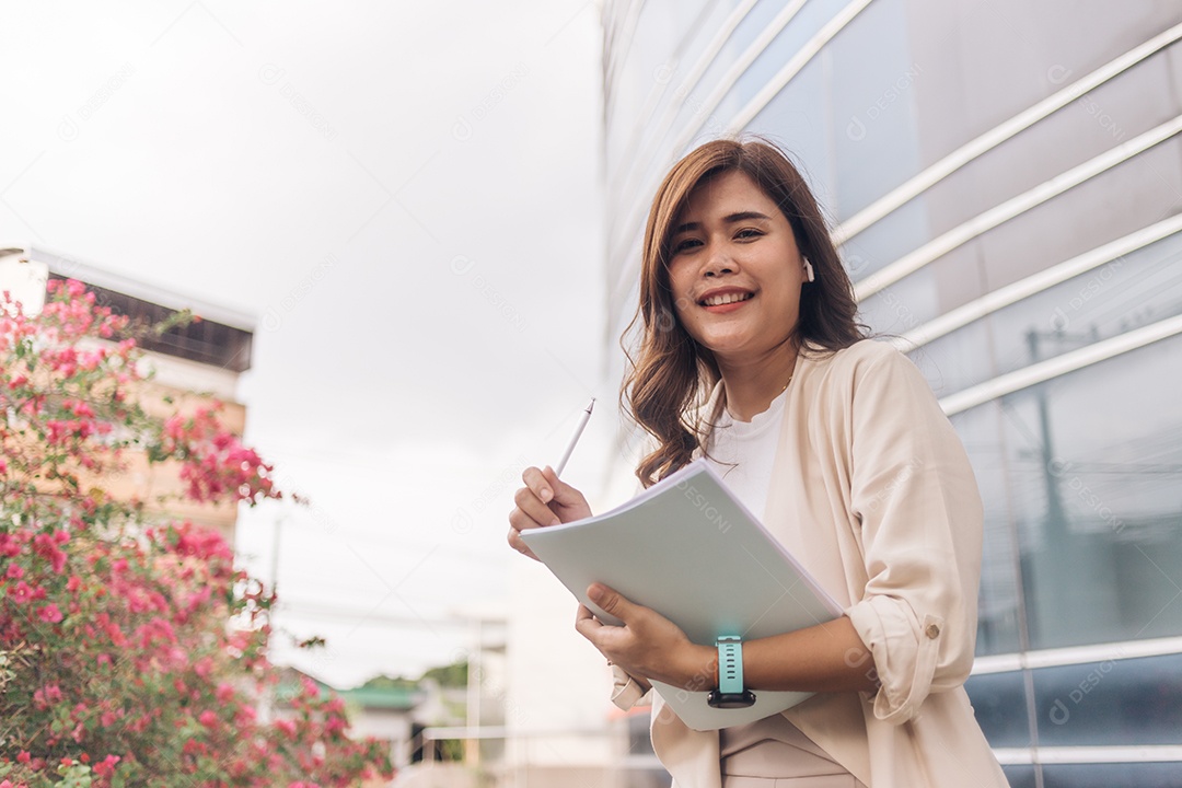Linda mulher de negócios asiáticos segurando um caderno e uma caneta na cidade.