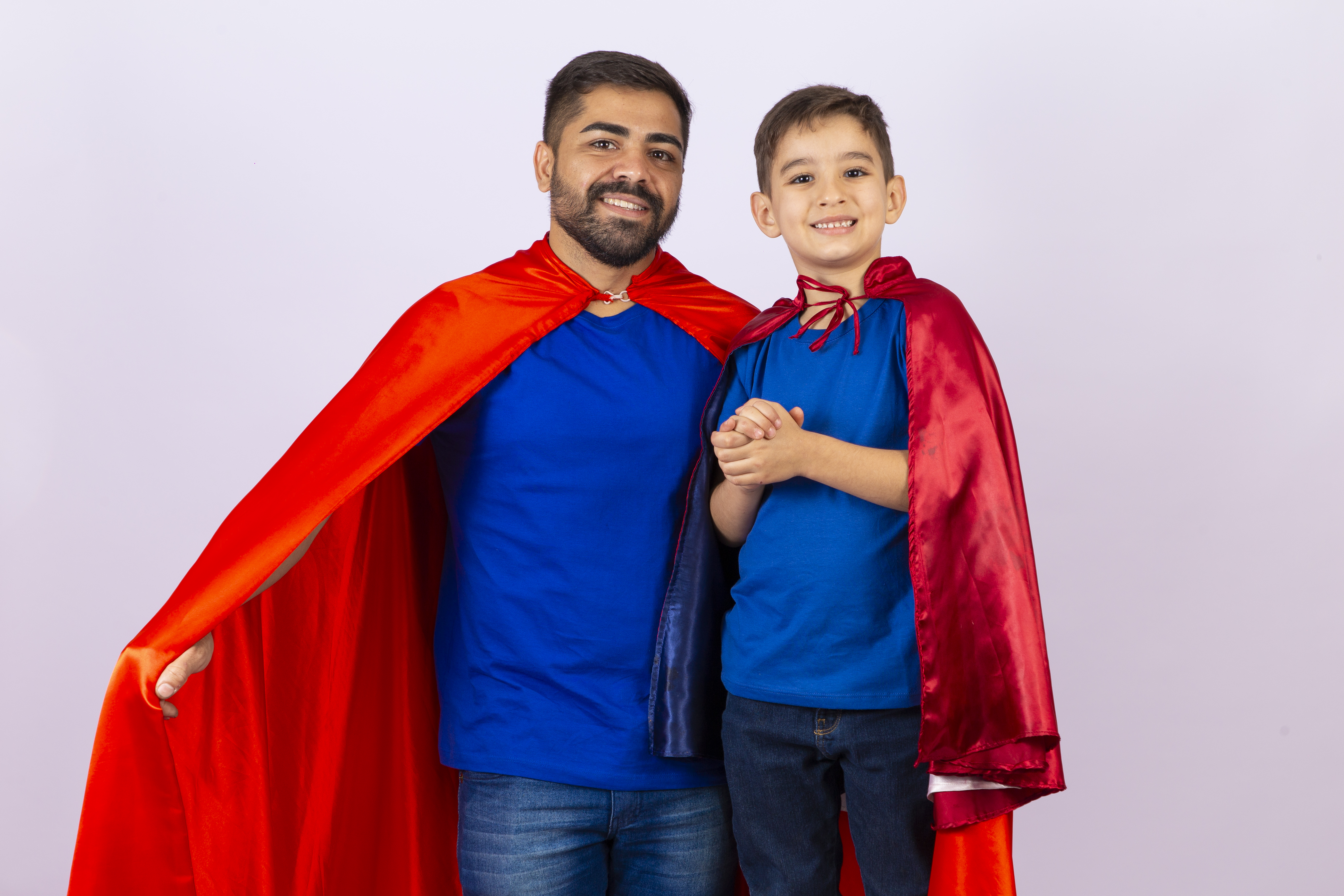 Pai e filho de com capa de super herói em fundo branco