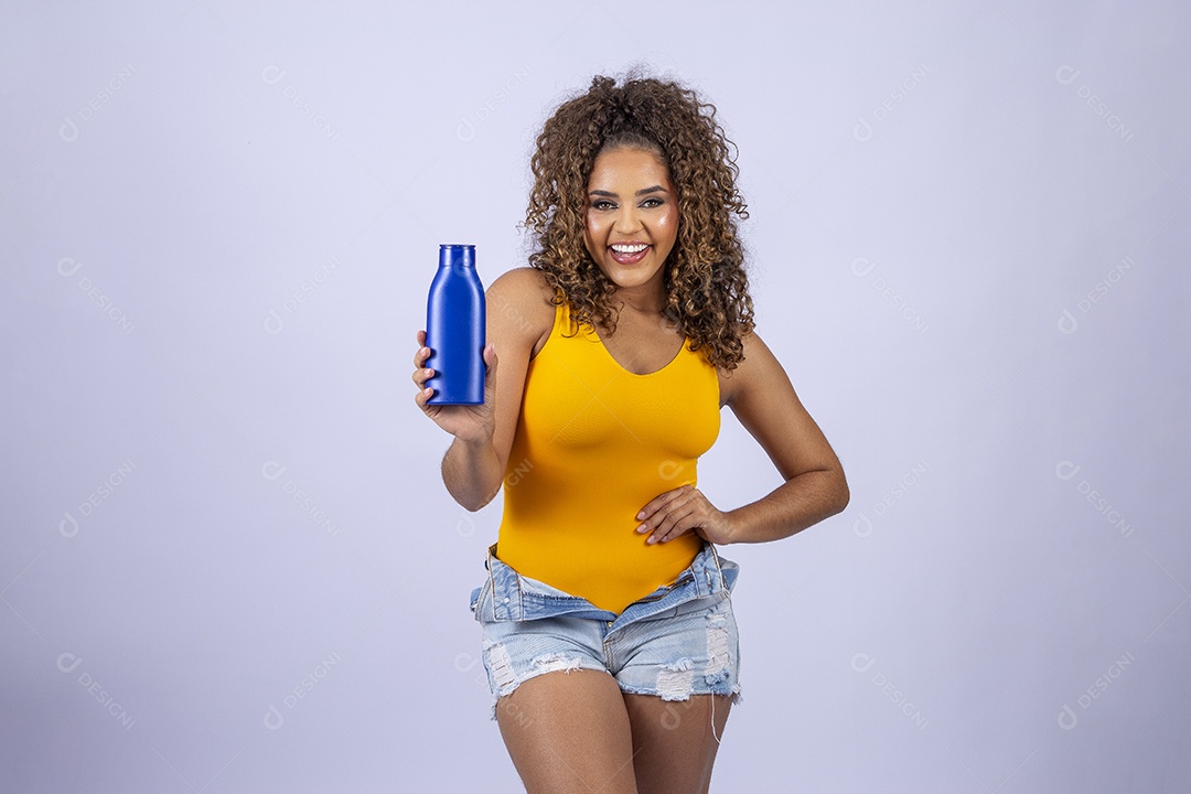 Linda mulher com maiô amarelo segurando frasco de hidratante corporal em fundo branco