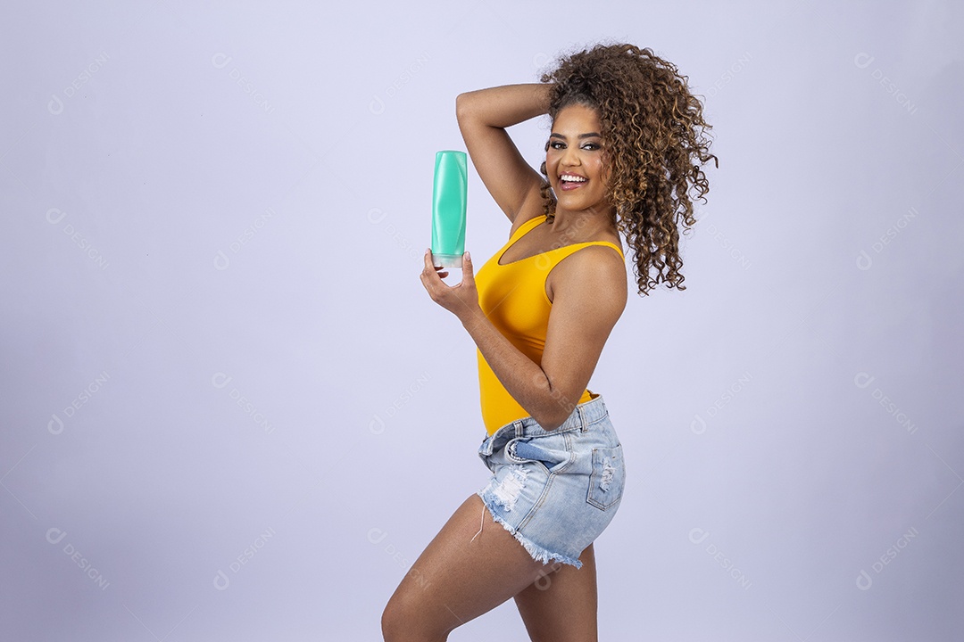 Linda mulher com maiô amarelo segurando shampoo de cabelo em fundo branco