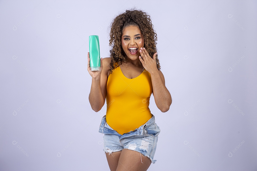 Linda mulher com maiô amarelo segurando shampoo de cabelo em fundo branco