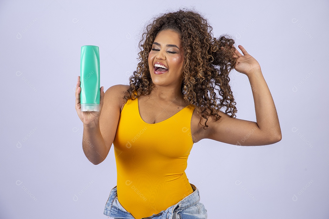 Linda mulher com maiô amarelo segurando shampoo de cabelo em fundo branco