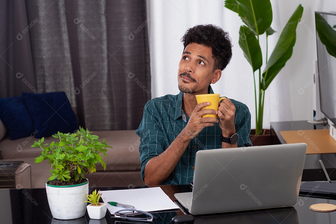 Jovem negro fazendo home office durante o dia na mesa com laptop