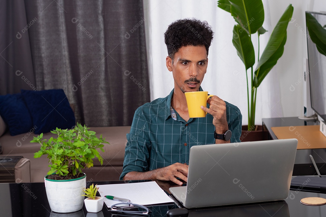 Jovem negro fazendo home office durante o dia na mesa com laptop