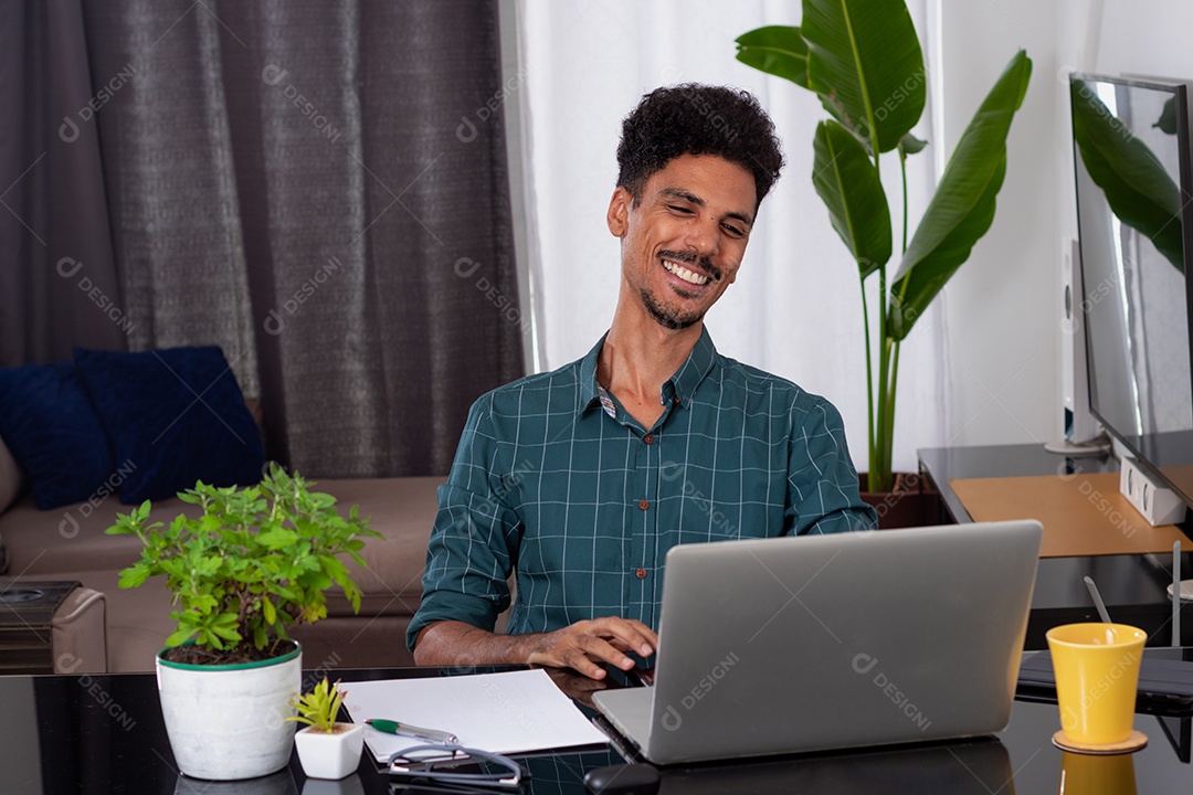 Jovem negro fazendo home office durante o dia na mesa com laptop